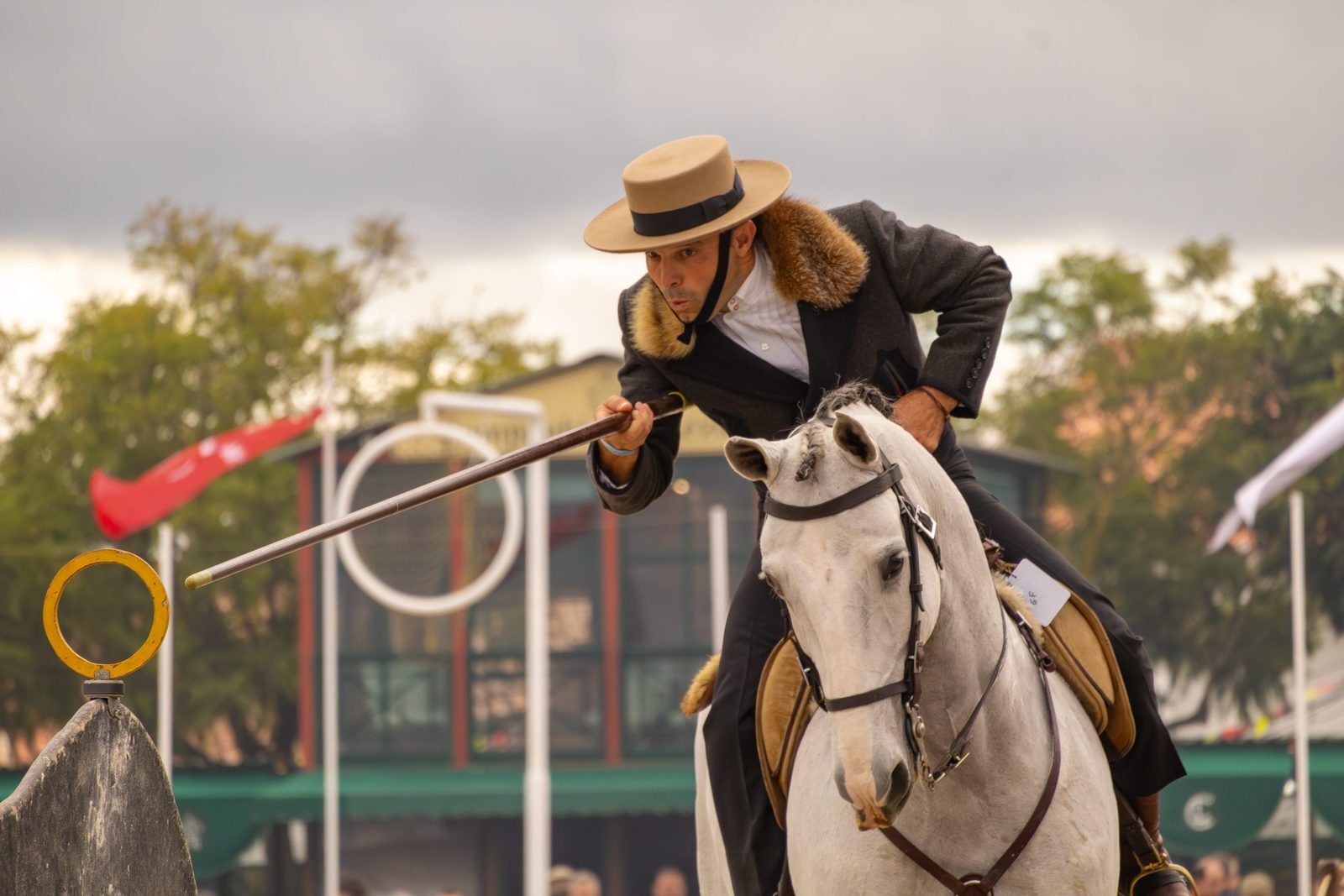 Ein Working-Equitation-Reiter führt im Wettkampf eine Stange zum Ringhindernis auf einem Schimmel-Lusitano